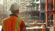 © Korn - Construction worker in safety gear looking at a large building under construction.