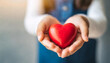 © Your Hand Please - little girl's hand gently holds a bright red heart against a clean, empty, blurred wall background, symbolizing innocence, love, care, and hope in a pure and simplistic manner