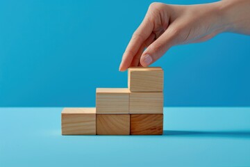 A hand is placing wooden blocks on top of each other, creating a stack. The blocks are of different sizes and are arranged in a way that they seem to be building something