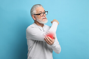 Wall Mural - Senior man suffering from pain in elbow on light blue background