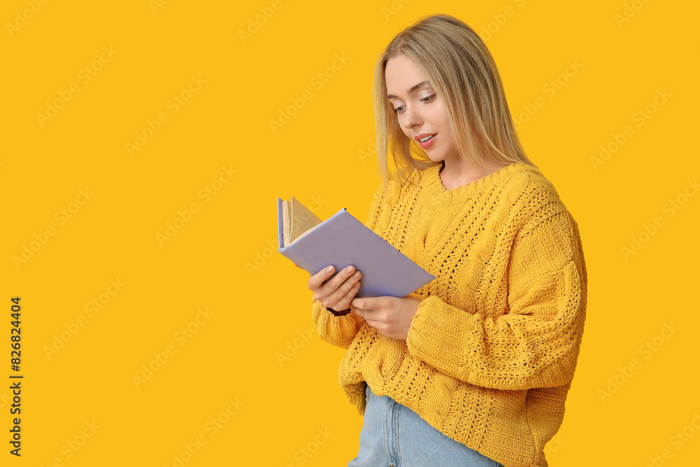 Beautiful young woman reading book on yellow background