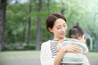 © kapinon - 新緑の公園で赤ちゃんを抱く母親　幸せや幸福、見守り、守る母性のイメージ