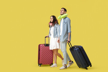 Wall Mural - Beautiful young happy couple of tourists with suitcases and travel pillows on yellow background