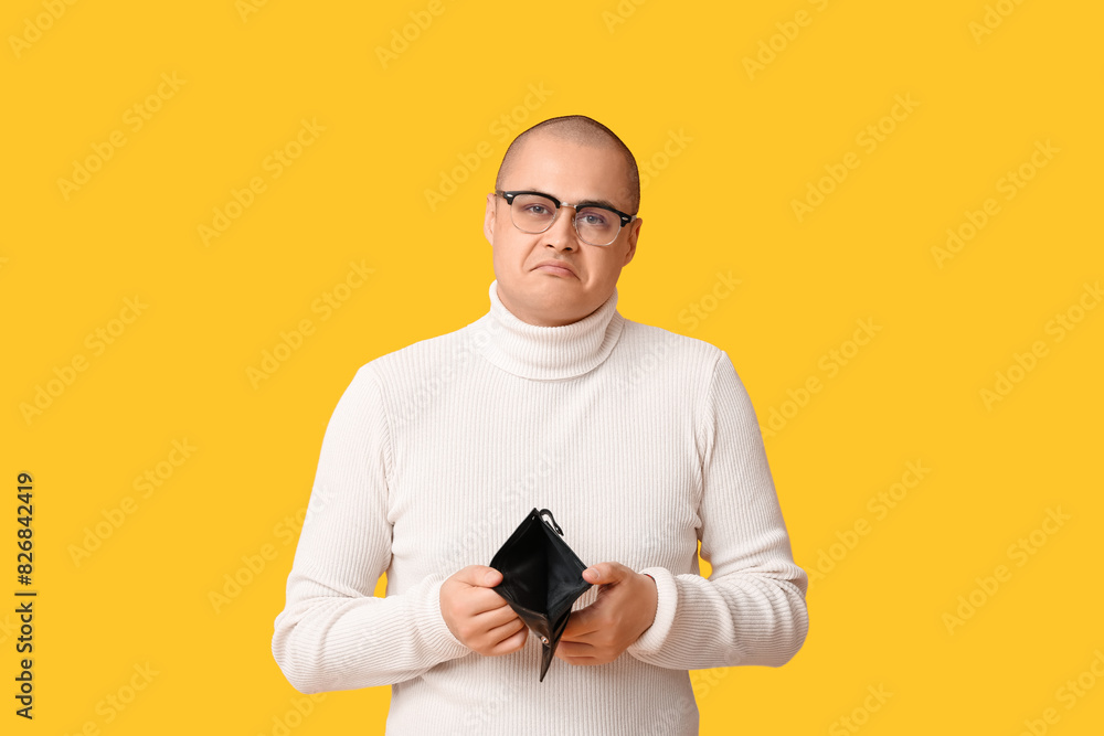 Sad young man with empty wallet on yellow background