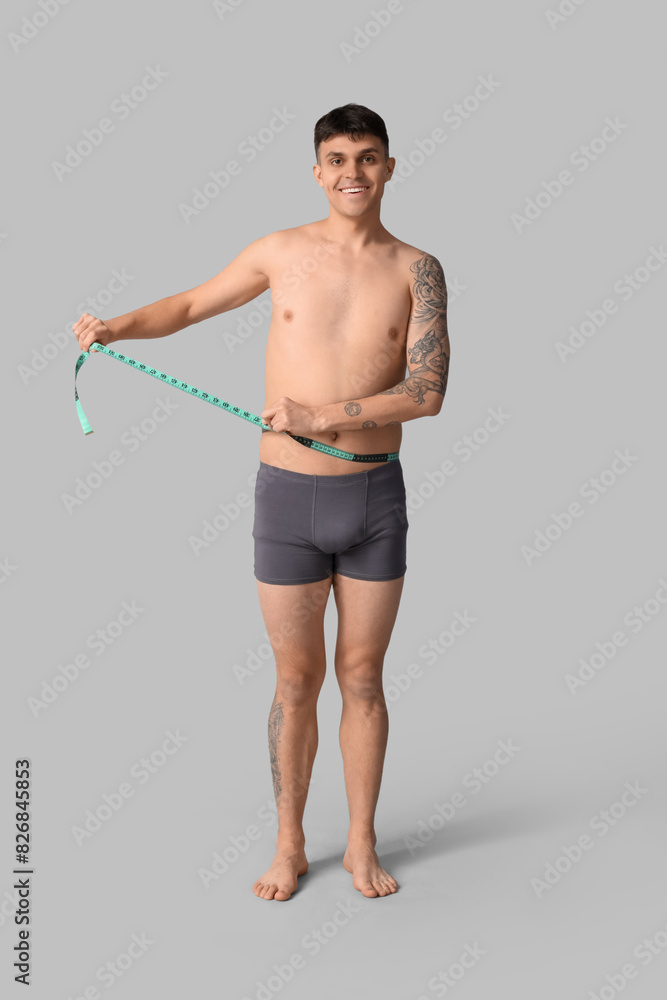 Young man with measuring tape on grey background. Weight loss concept