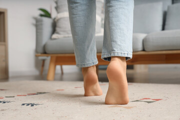 Poster - Barefoot woman walking on carpet at home, back view