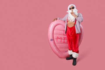 Sticker - Santa Claus with swim mattress showing silence gesture on pink background. Christmas in July