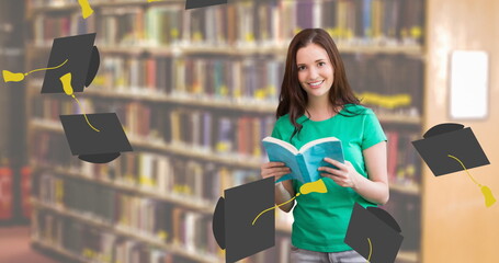 Canvas Print - Caucasian student holding book, wearing green t-shirt, smiling in library