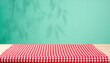 © Giuseppe Cammino - Empty wooden deck table and red checked tablecloth over mint wallpaper background