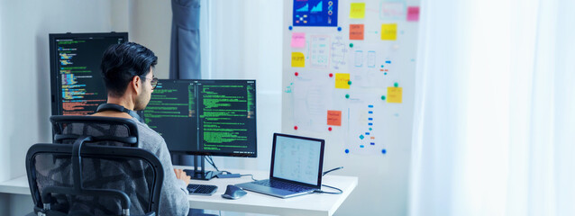 Asian software developers working on multiple screens displaying code and application diagrams in a modern office