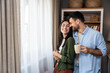 © Srdjan - Young happy couple standing near window in their new home looking out, talking about neighbors, enjoying new life in quiet community. Man and woman enjoying new life at their new house.