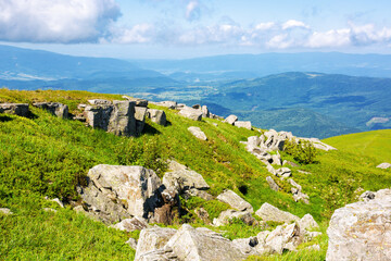 Wall Mural - stones and boulders on the green alpine hill. mountainous landscape of ukrainian carpathians in summer. spectacular view in to the distant rural valley beneath a blue sky with clouds on a sunny day