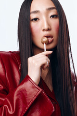 Wall Mural - Stylish young woman with black hair and red jacket enjoying a lollipop candy portrait