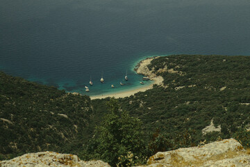 Sticker - a group of boats on the water near a beach and a rocky shore