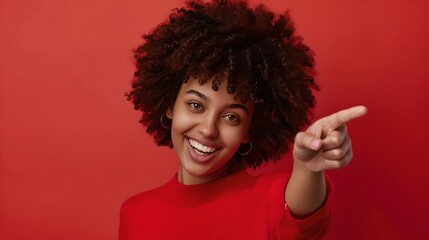 Poster - Smiling young woman pointing finger at camera on red background. Happy and friendly expression. AI