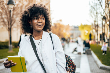 Beautiful and happy Black female student enjoying outdoors in college campus while study for the faculty exam.