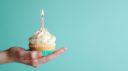 A hand delicately holds a cupcake adorned with a flickering candle