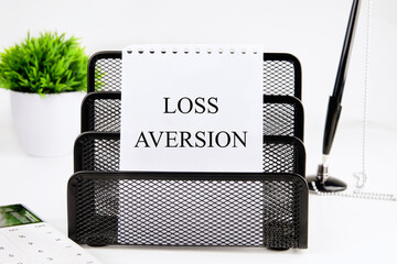 LOSS AVERSION text written on a blank sheet in a black stand on a white background