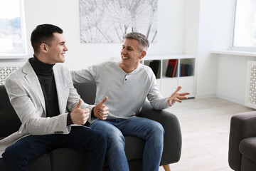 Poster - Happy men talking while sitting on sofa at home