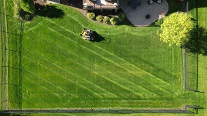 Wall Mural - Aerial view of riding lawn mower precisely cutting grass in a garden on a beautiful sunny day