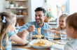 © Kien - A happy family eating pasta together at the dining table, the dad is holding a fork with macaroni in his hand and smiling at his wife