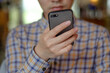 © Doublelee - Close-up of a young East Asian man’s light-skinned hand holding a mobile phone, with his face blurred as he reads the screen. Concept of technology usage, social media addiction and internet browsing.