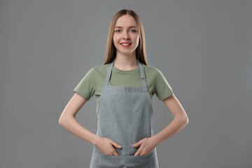 Wall Mural - Beautiful young woman wearing kitchen apron on grey background. Mockup for design