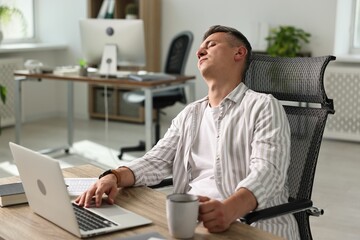 Wall Mural - Man with cup of drink snoozing at wooden table in office