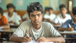 © Graphic Master - Indian male student looking at camera while writing in classroom