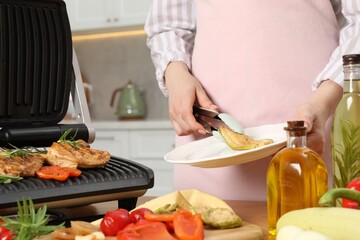 Wall Mural - Woman cooking different products with electric grill at wooden table in kitchen, closeup