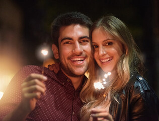 Wall Mural - Portrait, happy couple and sparklers at night for party, celebration and event together outdoor in city with light. Face, man and woman with fireworks on holiday, romantic date or laugh on vacation