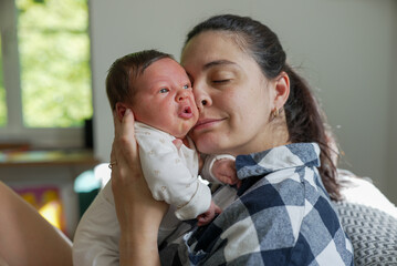 Mother holding newborn baby close to her face, both in a calm and intimate moment, indoor scene with soft lighting, capturing the deep bond and love between mother and child, heartwarming