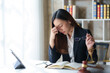 ©  NCST Studio - A female lawyer looking stressed while working in her office, holding glasses and touching her forehead.