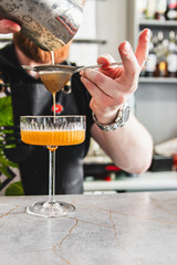 Wall Mural - A skilled bartender pours a cocktail through a strainer into an elegant glass on a bar counter