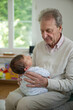 © Marco - Senior man sitting indoors, cradling a baby in his lap, looking down with a loving and thoughtful expression. The bond between the generations is clearly visible in this intimate scene