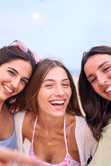 Wall Mural - Vertical Portrait cheerful group of three attractive European women posing photo on beach. Smiling friends looking at camera. Gen z joyful female outdoor summer holiday