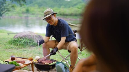 Wall Mural - Group of Happy Asian man and woman enjoy and fun outdoor lifestyle travel nature camping in forest on summer vacation. People friends having dinner eating bbq grill and drinking beer together at night