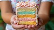 © aicandy - A close-up view of a colorful four-layer cake slice held by a person, showcasing pastel-colored layers and a piped frosting top, emitting a delightful and inviting appearance