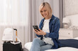 © New Africa - Smiling guest with smartphone relaxing on bed in stylish hotel room