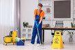 © New Africa - Cleaning service worker washing floor with mop. Bucket with supplies and wet floor sign in office