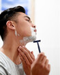 © peopleimages.com - Razor, man and shaving face in bathroom for hair removal, health or wellness with cosmetic foam on morning routine in home. Cream, beard and cut for skincare, grooming or clean in profile for hygiene