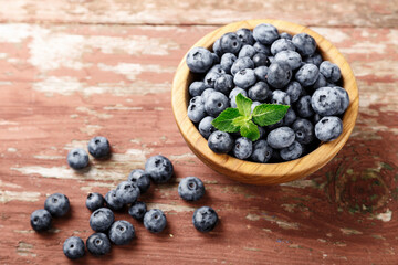 Wall Mural - Blueberry berries with mint leaves are in a wooden plate on wooden background.