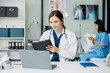 © Nuttapong punna - Young female doctor in white medical uniform using laptop and tablet talking video conference call at desk,Doctor sitting at desk