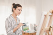 © pitipat - Portrait photo of young beautiful Asian woman artist painting water color art picture in indoor studio.