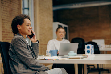 Wall Mural - Female manager is talking phone with client while sitting in coworking on colleague background