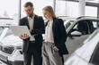 © anatoliycherkas - A male salesman showing something on a laptop to a female client buying a car inside a car dealership