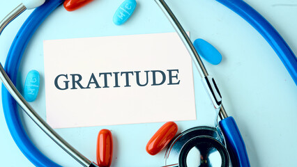 Concept GRATITUDE written on a white business card on a blue background with a stethoscope, pills in a composition in cold tones