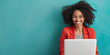 © Armin - A smiling woman stands in front of a teal blue background working on a laptop, expressing productivity and modern work culture suitable for stock websites.