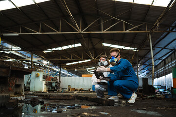 A team of engineers wearing safety suits and gas masks is under inspection of a chemical tank at an industrial site.