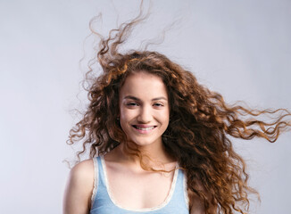 Portrait of a gorgeous teenage girl with curly hair, blowing in wind. Studio shot, white background with copy space